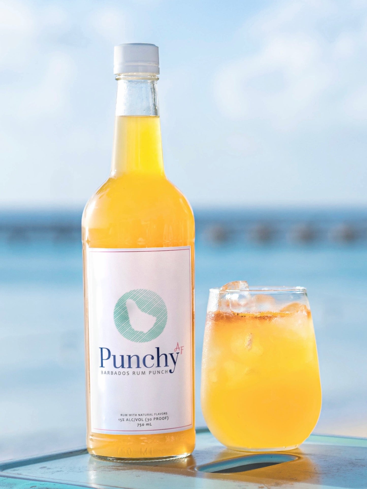 Bottle and glass of Punchy AF with a beach background
